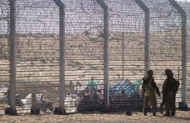 African refugees sit on the ground behind a border fence after they attempted to cross illegally from Egypt into Israel as Israeli soldiers stand guard near the border with Egypt, in southern Israel, Tuesday, Sept. 4, 2012. Israel is staunching the flow of African migrants who have poured into the Jewish state by the tens of thousands, rapidly building a border fence and implementing a new policy of detaining Africans upon arrival. Israels army says over the past few days, a group of African migrants has waited on the Egyptian side of the fence. Israeli soldiers are providing the group with water, but not allowing them into Israel.(AP Photo/Ariel Schalit)