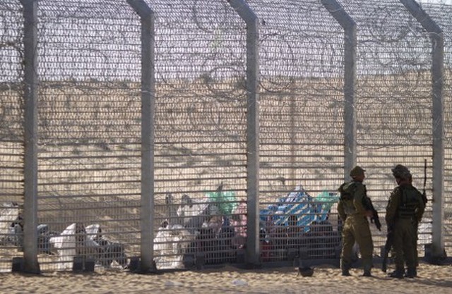 African refugees sit on the ground behind a border fence after they attempted to cross illegally from Egypt into Israel as Israeli soldiers stand guard near the border with Egypt, in southern Israel, Tuesday, Sept. 4, 2012. Israel is staunching the flow of African migrants who have poured into the Jewish state by the tens of thousands, rapidly building a border fence and implementing a new policy of detaining Africans upon arrival. Israels army says over the past few days, a group of African migrants has waited on the Egyptian side of the fence. Israeli soldiers are providing the group with water, but not allowing them into Israel.(AP Photo/Ariel Schalit)